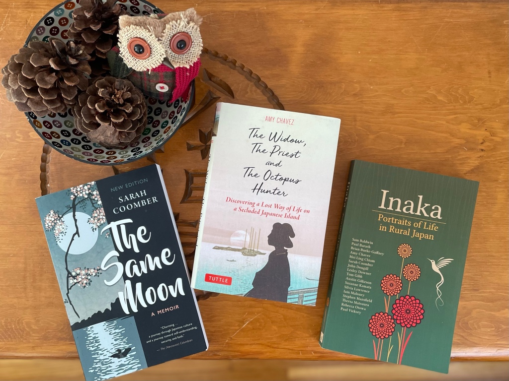Three books -- The Same Moon, The Widow the Priest and the Octopus Hunter, and Inaka ... plus a bowl containing pine cones and a stuffed owl.