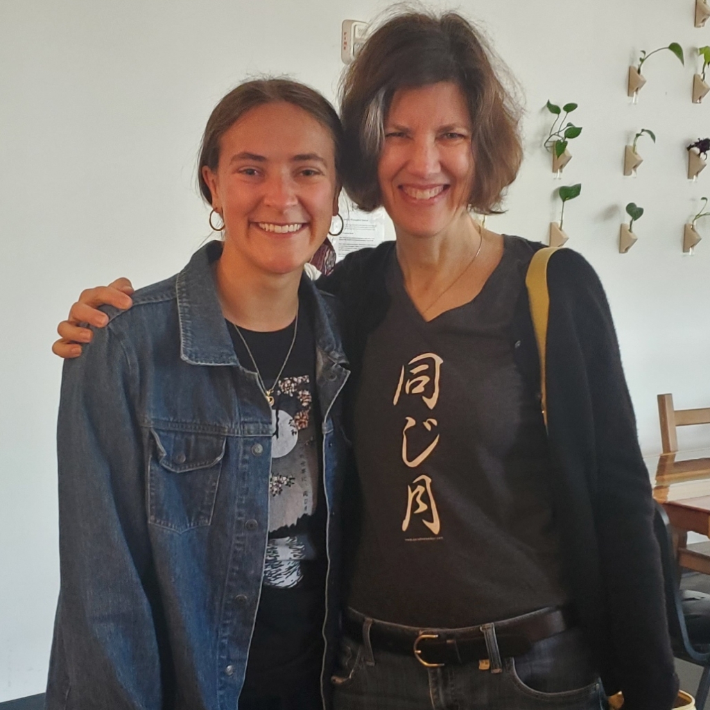 Two women wearing T-shirts -- one with a moon, cherry blossoms and Japanese script, the other with three Japanese characters that mean "Same Moon"